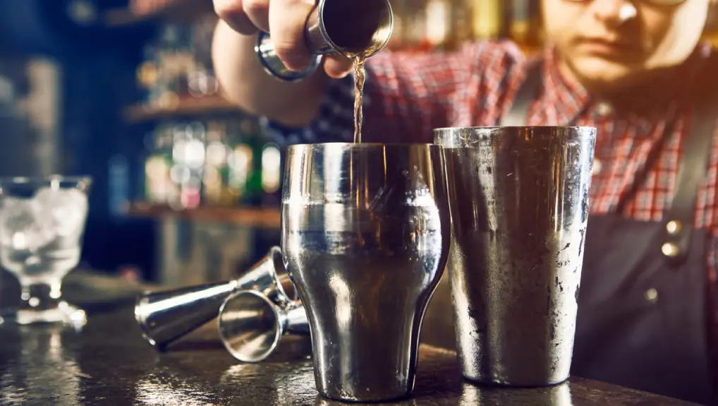 close up image of a bar setting with a bartender pouring a drink from a stylish cocktail shaker.