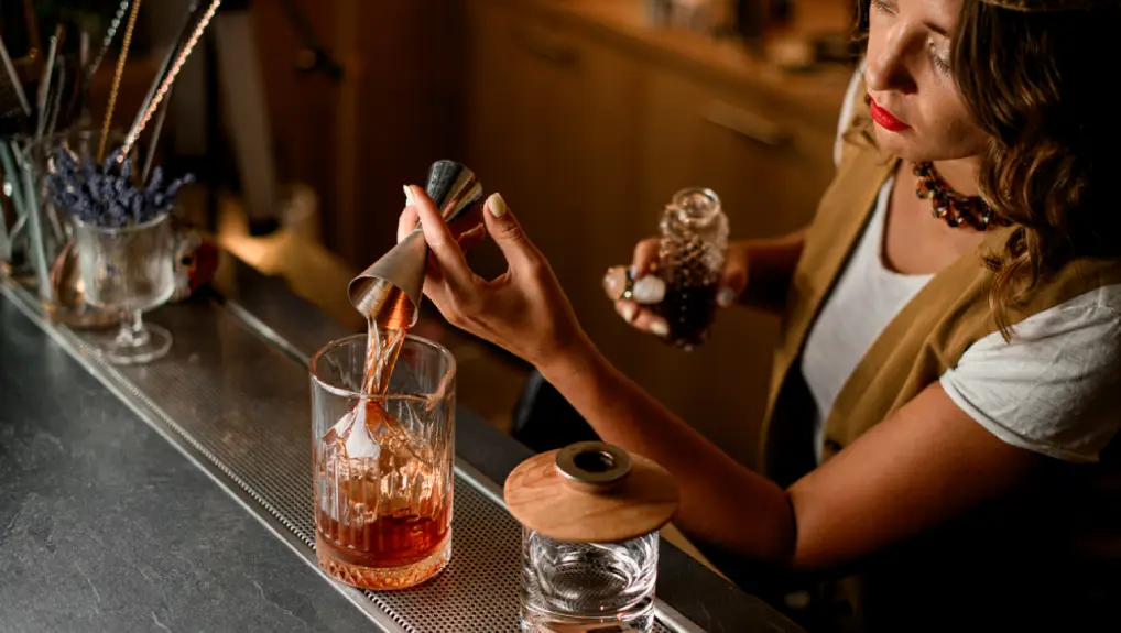 image of cocktail bar with female bartender using a mixing glass ideal bar tools for beginners to produce a cocktail