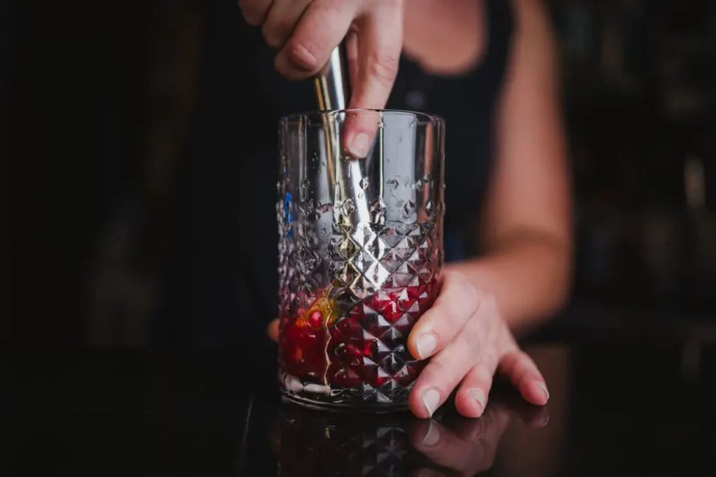 close up image of a cocktail muddler ideal bar tools for beginners being used to create a cocktail in a highball glass.