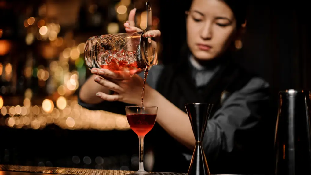 image of female bartender using a strainer while producing a cocktail. Ideal bar tools for beginners