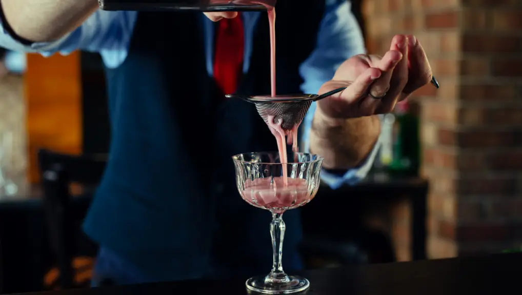 close up image of a bartender using a fine mesh strainer to produce a cocktail