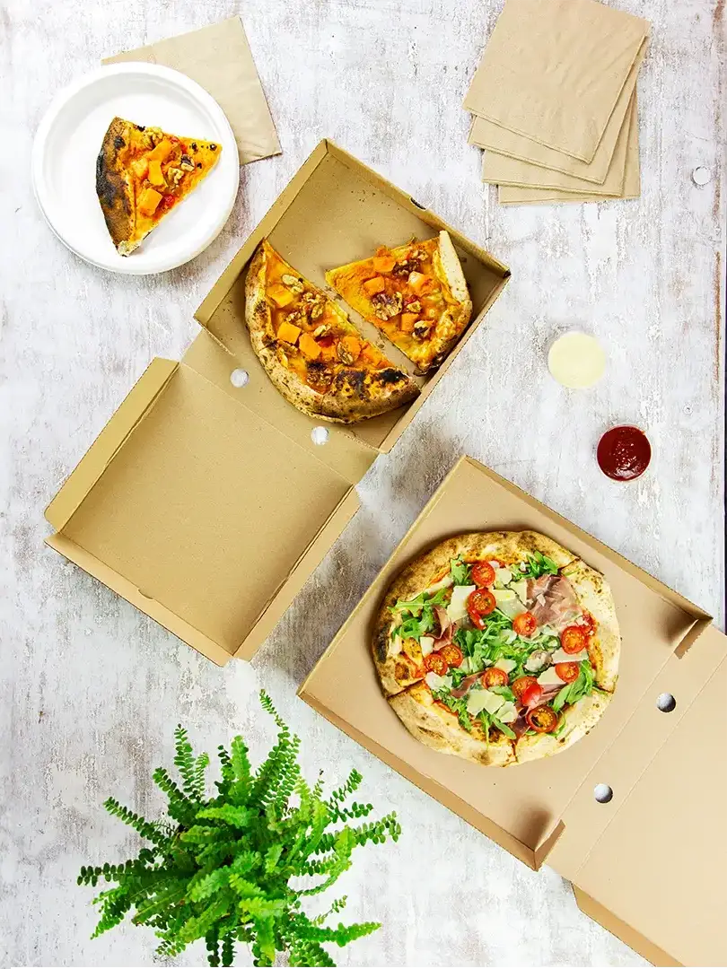 Image of a table top packed with various pizzas sitting on disposable pizza boxes in a takeaway environment