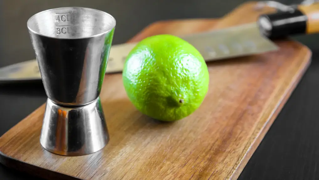 Close up image of a jigger, chopping board and knife part of a professional bartenders toolkit.