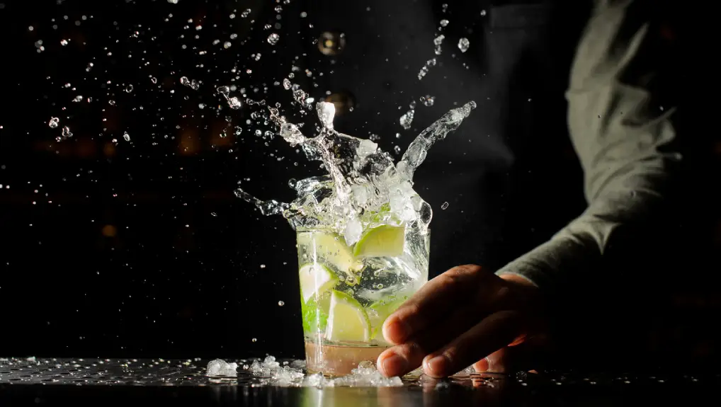 close up image of ice cubes splashing in a cocktail glass in a bar 