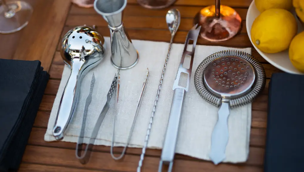 Close up image of must have bar tools for crafting cocktails including strainer, jigger.