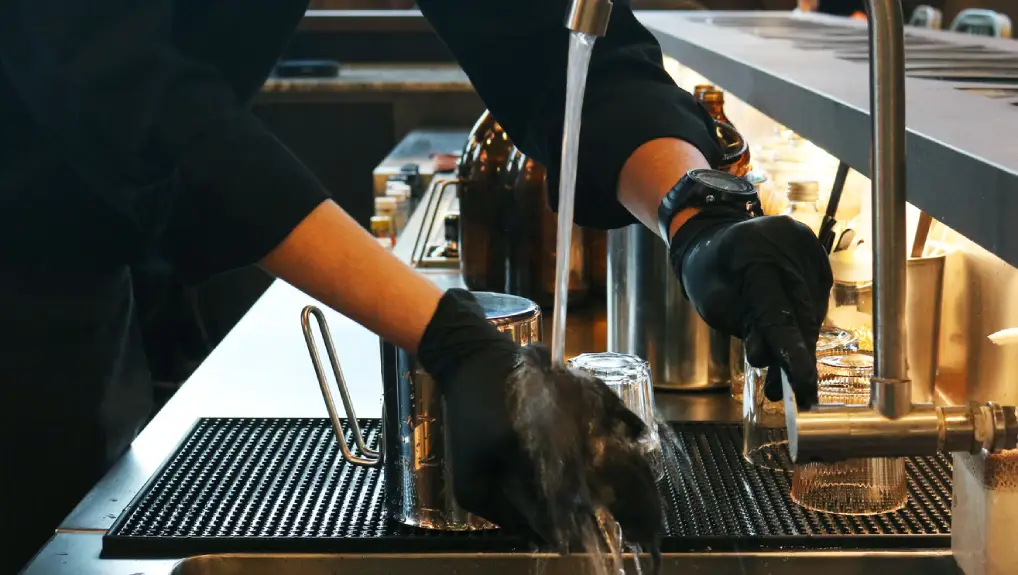 Close up image of a bartender wearing latex gloves carrying out bar maintenance to help maintain the bar equipment for a longer life