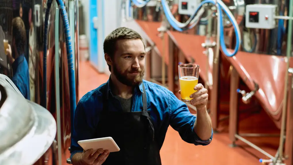 Image of a bartender during keg line checks the bartender is holding a pint glass with a beverage inside and in the other hand he is holding a clip board.