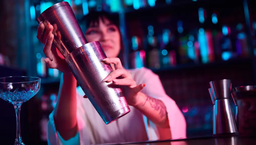 Image of bartender knowing which shaker to use the boston shaker the setting is in a bar with a rose light filter 