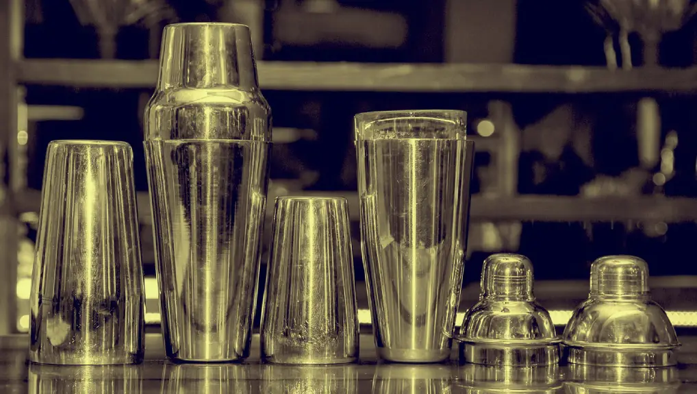 Close up image of a collection of stainless steel cocktail shakers on a bar the lighting is silver tinted