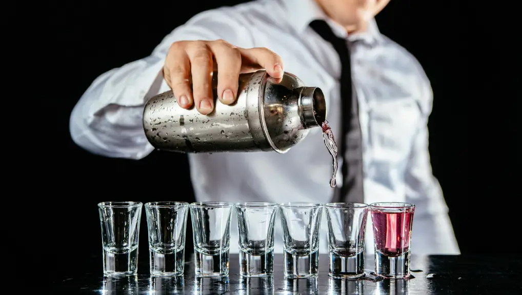 Close up image of a bartender pouring from a cobbler cocktail shaker in a bar