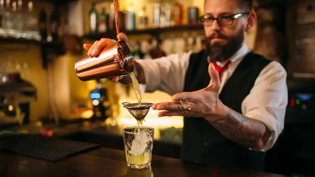 Close up image of a bartender pouring from a French cocktail shaker in a trendy bar