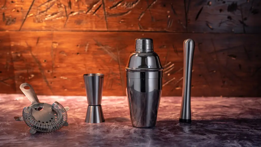 Close up studio image of a cobbler cocktail shaker along with a jigger, strainer and muddler