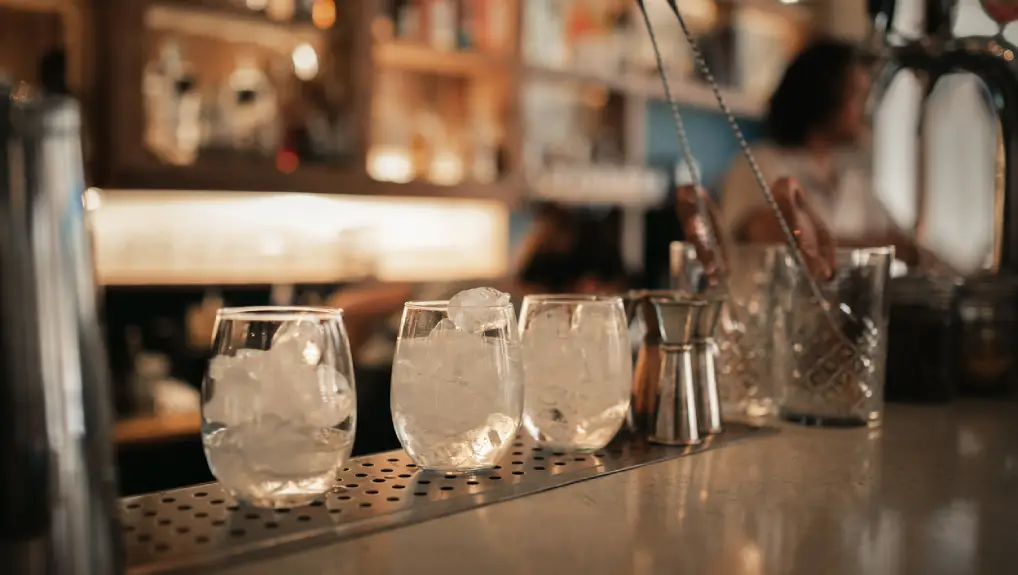 Close up image of three glasses filled with ice on a bar top in a small commercial bar.