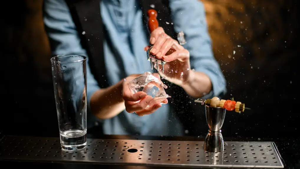 Close up image of a bartender in a small commercial bar using ice tools