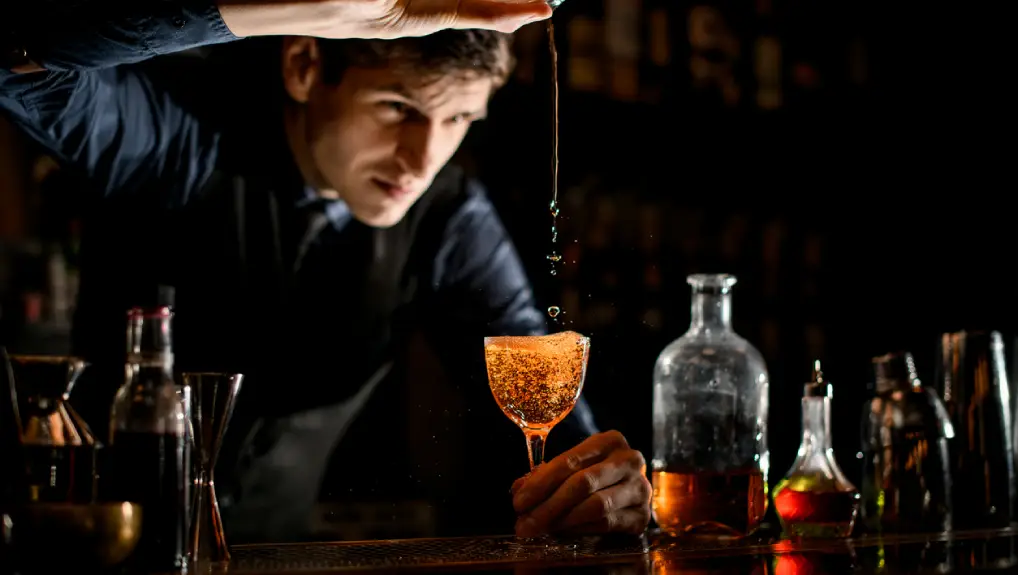 Image of a bartender creating a cocktail in a darkly lit bar